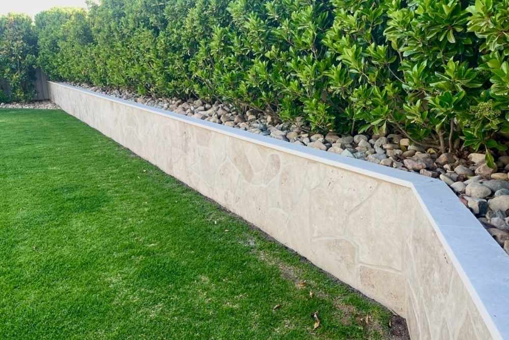 A professional limestone textured retaining wall bordering a lush green lawn and garden hedge in Wagga Wagga